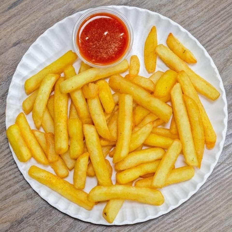 A white plate filled with golden french fries and a small cup of red ketchup.