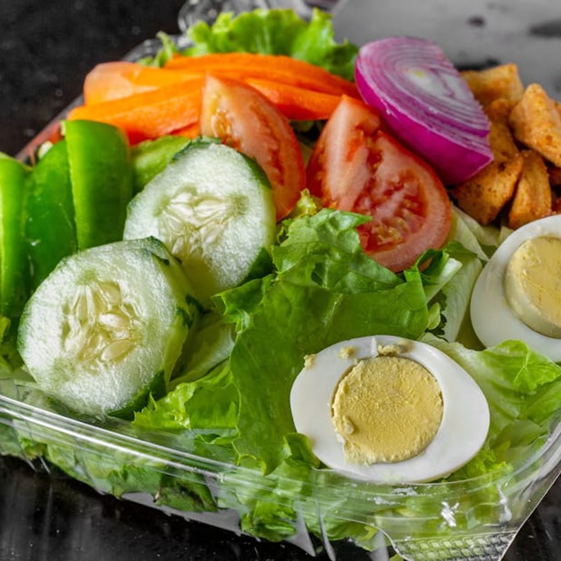Fresh garden salad with lettuce, cucumbers, tomatoes, carrots, red onion, croutons, and hard-boiled eggs.